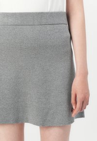 Gonna grigia in maglia con una consistenza morbida, caratterizzata da un taglio dritto e una cintura in vita. L'orlo è leggermente svasato con una finitura a taglio vivo.