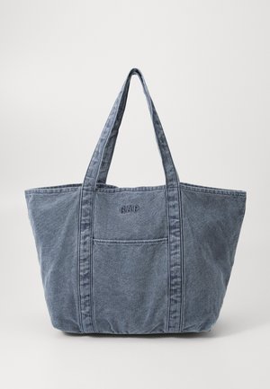 Blå denim tote taske med lange håndtag, frontlomme og broderet "GAP" logo centreret over lommen.