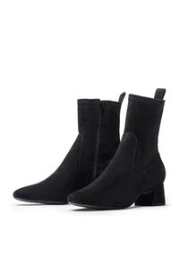 Stivaletti neri in suede con cerniere laterali, punta affusolata e tacco basso su uno sfondo bianco.