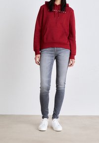 Rode hoodie met een voorzak en trekkoord, gecombineerd met grijze skinny jeans en witte sneakers. Eenvoudig ontwerp, casual materiaal.