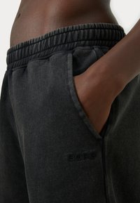 Juoda sportinė kelnė, pagaminta iš minkštos medžiagos, su elastinga juosmens juosta ir šoninėmis kišenėmis. „BORG“ logotipas įspaustas šalia kišenės.