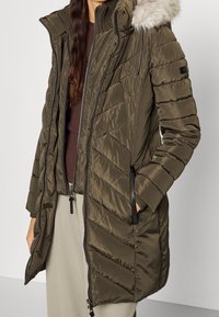 Olivgrön isolerad parka med avtagbar konstpälsluva, dragkedjestängning framtill och diagonalt quiltat mönster. Har sidofickor och ribbade ärmslut.