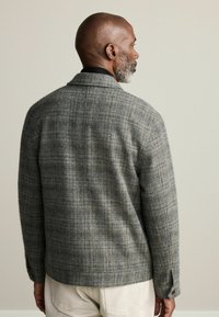 Gray plaid blazer in textured fabric with a notched collar, back vent, and buttoned cuffs. Features a relaxed fit and tailored silhouette.