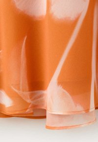 Tissu fluide orange et blanc avec des motifs lumineux abstraits, montrant les détails de l'ourlet et des superpositions translucides sur le bord inférieur.