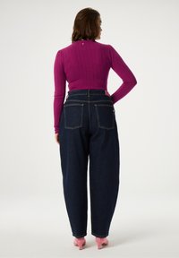 Fuchsia geribbelde langemouwen top gecombineerd met hoog-taille donkere denim wijde broek en roze kittenheels. Opvallende details aan de achterkant zijn de zakken.