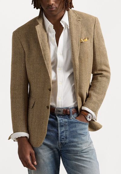 Brown herringbone blazer with notch lapels, paired with a white shirt and blue jeans. Features a folded yellow pocket square and watch.