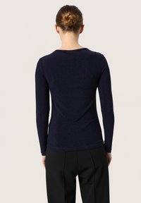 Navy long-sleeve top in a sparkly knit fabric, featuring a rounded neckline and fitted silhouette, paired with black high-waisted trousers.