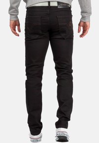 Jean en denim noir à coupe slim, avec des poches arrière ornées de coutures et d'une étiquette de marque, associé à des baskets blanches.