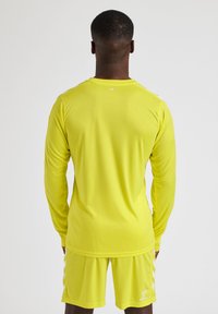 Langærmet sports-T-shirt og shorts i klar gul, med en glat tekstur og simpelt design. Inkluderer kontrasterende hvide accenter.