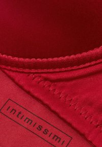 Rote Unterwäsche aus glattem Satinstoff. Auffällige Picot-Bordüre und Nähdetails entlang der Naht. Das Etikett trägt den Schriftzug "Intimissimi" in Schwarz.