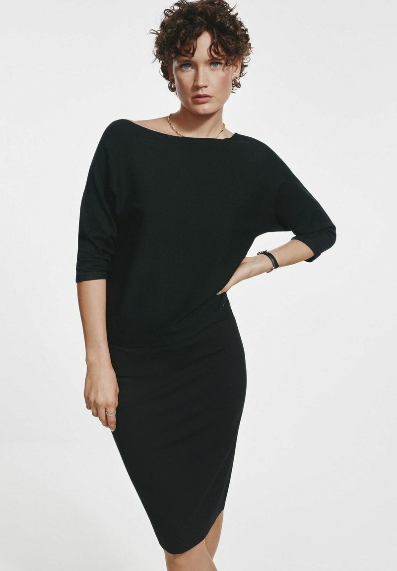 Czarna sukienka z rękawami do trzech czwartych, dopasowanym krojem, miękką teksturą i asymetrycznym dołem. Posiada szeroki dekolt i minimalistyczne detale.