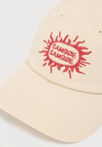 Μπεζ βαμβακερό καπέλο με στρογγυλεμένη σκοπευτική άκρη. Διαθέτει κεντητό κόκκινο λογότυπο "SAMSØE SAMSØE" σε σχέδιο ηλιοφάνειας. Ορατές ραφές.
