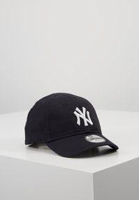 Crna pamučna bejzbol kapa s bijelim izvezenim "NY" logotipom, zakrivljenim vizirima i podesivim remenom straga.