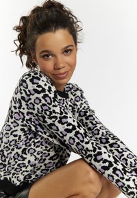 Sweter w wzór leopardzi w kolorach czarnym, białym i lawendowym, z prążkowanym dołem i miękką dzianiną. Modelka pozująca z rękami skrzyżowanymi.