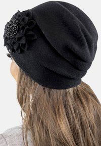 Bonnet en tricot noir avec un tissu texturé et des embellissements floraux ornés de perles. Design doux et ample qui tombe à l'arrière.