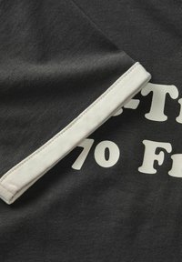 Tmavě šedá tričkovina s kontrastním bílým nápletem a tučným bílým textem "70." Hladká textura, design s krátkým rukávem.