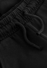 Fekete fleece melegítőnadrág, állítható derékkal, bordázott textúrával és puha anyaggal. A tervezés a kényelemre és a funkcionalitásra összpontosít.