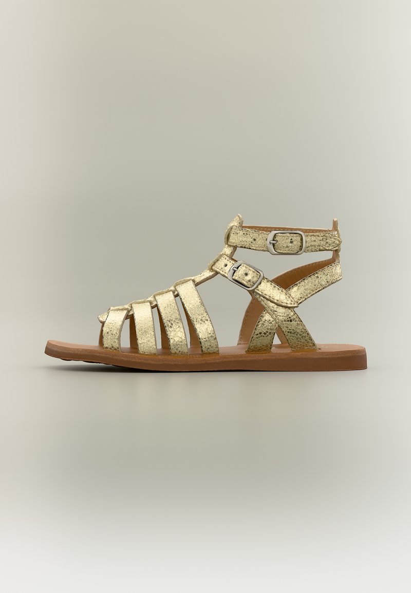 Επίπεδο χρυσό μεταλλικό σανδάλι γλαδιόρα με πολλαπλές λουριά και δύο ρυθμιζόμενες αγκράφες σε καφέ σόλα, πλάγια όψη.