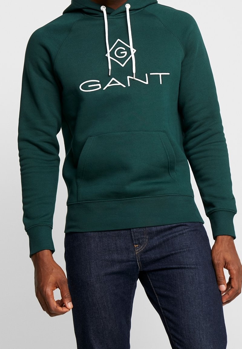 Sudadera de algodón verde con un logo blanco de "GANT", bolsillo frontal y cordones ajustables. Puños y dobladillo acanalados para un ajuste ceñido.