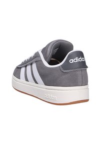 Szare sneakersy Adidas z białymi pasami, białą podeszwą i brązową podeszwą zewnętrzną, pokazane z tylnego kąta.