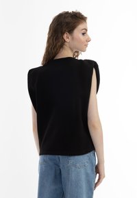 Sort ærmeløs top med strukturerede skuldre, lavet af glat materiale. Kombineret med lyseblå denim bukser, som har en afslappet pasform.