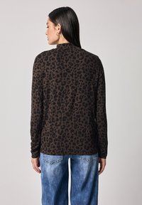 Langarmhemd in Braun mit schwarzem Leopardenmuster, mit lockerer Passform und rundem Ausschnitt. Kombiniert mit hellblauen weitbeinigen Jeans.