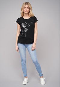 Svart bomull t-skjorte med korte rullede ermer og grafikken av hvit løvetann. Kombinert med lyseblå skinny jeans og hvite sneakers.