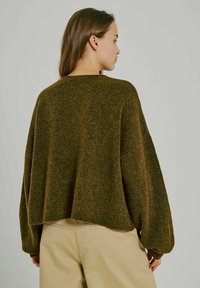 Brązowy, oversize sweter z dzianiny o szerokim dekolcie, opadających ramionach i długich rękawach. Tkanina ma miękką, teksturowaną powierzchnię.