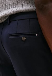 Pantaloni navy con una trama liscia, dotati di una tasca posteriore con chiusura a bottone e un delicato accento a motivo.