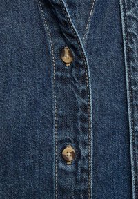 Denim shirt featuring a deep blue color, contrasting stitching, and round metal buttons along the front. Detail of fabric texture visible.