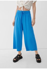 Blauwe wijde broek met een elastische tailleband, voorzien van een trekkoord. Gecombineerd met zwarte platformsandalen. Gladde, lichtgewicht stof.