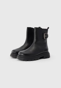 Bottines noires en cuir avec une finition lisse, des semelles en caoutchouc épaisses, une fermeture éclair sur le côté et une boucle décorative d'un côté.