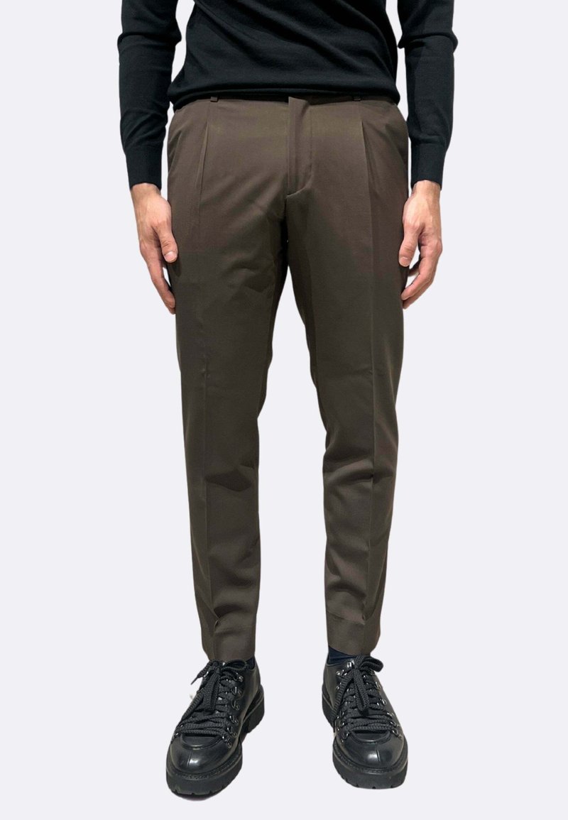 Chinos marroni da uomo con vestibilità slim, pancia piatta, tasche laterali e una delicata lucentezza, abbinati a sneakers nere con lacci.