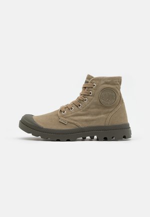 Bottes en toile montantes kaki avec embout en caoutchouc, lacets plats et semelle texturée. Présente un patch logo rond sur le côté.