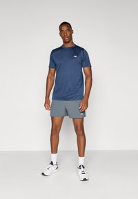 Marineblaue, kurzärmlige Sport-T-Shirt mit Rundhalsausschnitt und Logo. Tragen Sie dazu graue Shorts und weiße Schuhe mit schwarzen Akzenten.