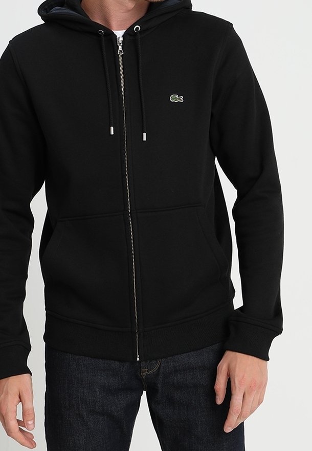 Sudadera con cremallera negra hecha de un tejido suave, con un logo verde en el lado izquierdo del pecho, que cuenta con capucha con cordones y bolsillos tipo canguro.