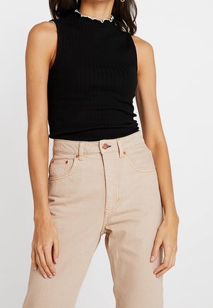 Musta, ribbineulottu hihaton paita, jossa on röyhelöinen kaulus, yhdistetty vaalean beigen vaaleisiin korkeavyötäröisiin farkkuihin, joissa on klassinen viiden taskun malli.