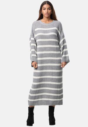 Kvinde iført en grå og hvid stribet strikket lang sweaterkjole med lange ærmer og sorte plateau-ankelstøvler.