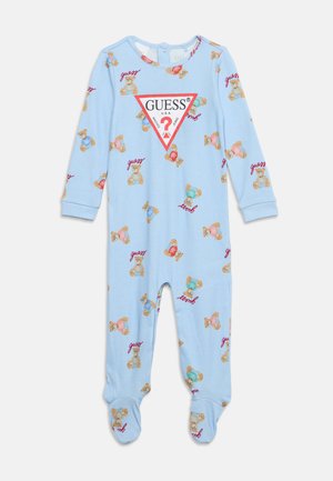 Barboteuse bleu clair pour bébé avec imprimé ours en peluche et logos rouges "Guess", avec un grand logo triangulaire "GUESS" sur la poitrine et pieds couverts.