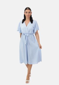 Vestido envolvente de color azul claro con mangas cortas y acampanadas, cintura ajustable con lazo y un dobladillo a la altura de la rodilla. Tejido suave con una superficie texturizada.