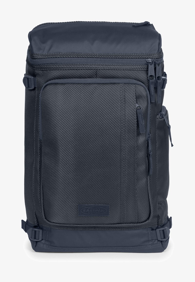 Tummansininen reppu, jossa on teksturoitu kangas, useita vetoketjullisia osastoja ja säädettävät hihnat. Varustettu tukevalla pohjalla ja vahvistetulla materiaalilla.