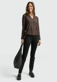 Long-sleeved, v-neck top in textured black and brown pattern, paired with black skinny jeans and chunky black loafers; holding a black bag.