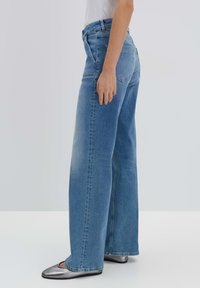 Jeans blu a vita alta e gamba larga in denim. Presentano un classico design a cinque tasche e una finitura sbiadita. Abbinati a ballerine metalliche.