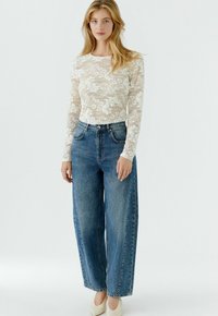 Lace long-sleeve top in off-white with floral pattern; loose-fitting blue denim jeans with high waist and straight leg; light-colored shoes.
