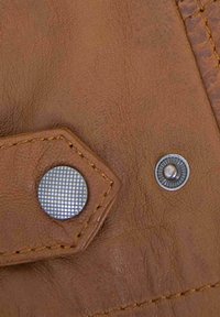 Brown textured leather surface featuring two metallic buttons—a flat, grid-patterned one and a round button with a ridged edge.