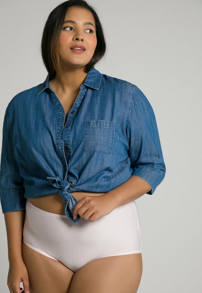 Camicia di jeans con maniche arrotolate, annodata in vita, abbinata a mutandine alte di colore rosa chiaro con sottili righe verticali.