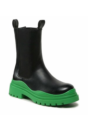 Czarny skórzany botek za kostkę z elastycznymi panelami po bokach i masywną zieloną gumową podeszwą z głębokim bieżnikiem, wyposażony w pętelki do ściągania z przodu i z tyłu.