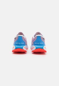 GORE-TEX tekaške čevlje z modrim mrežastim zgornjim delom in rdečim podplatom. Značilnosti vključujejo oblazinjen petni del in bele akcentne detajle v obliki.