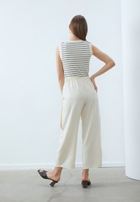 Striped sleeveless top in white and navy, paired with cream wide-leg pants, featuring an elastic waistband. Black heeled sandals.