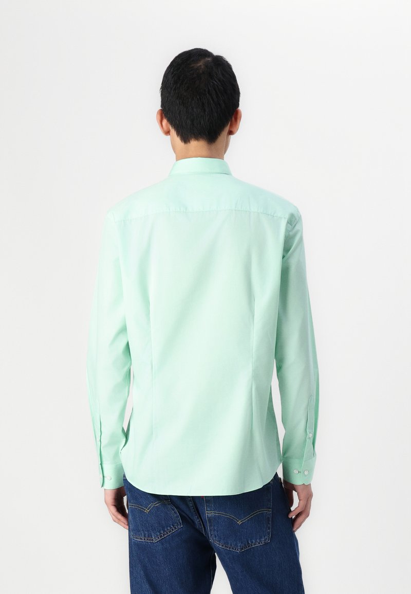 Camisa de botones verde menta con mangas largas, cuello puntiagudo y dobladillo curvado, combinada con pantalones de mezclilla azul oscuro.